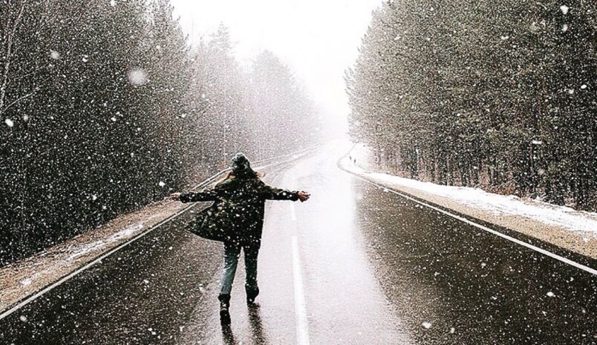 A woman is standing on a snowy road with her arms outstretched.