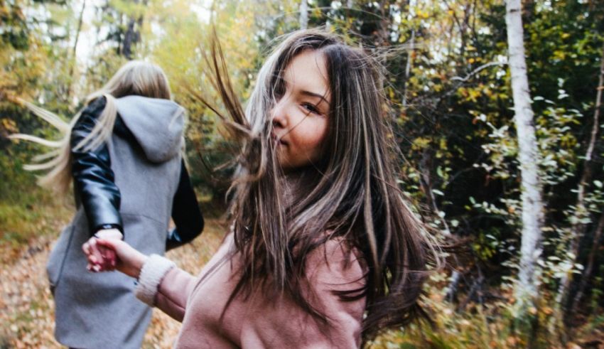 Two girls walking in the woods with their hair blowing in the wind.