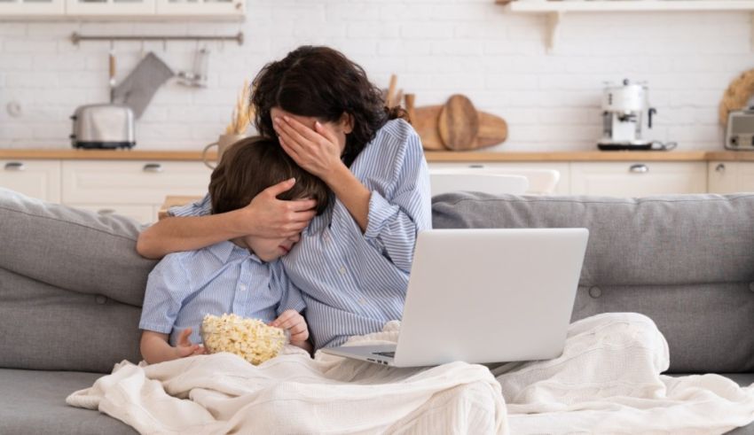 A woman and her son sitting on a couch with popcorn and a laptop.
