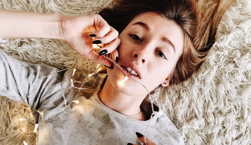 A girl laying on a rug with lights around her neck.