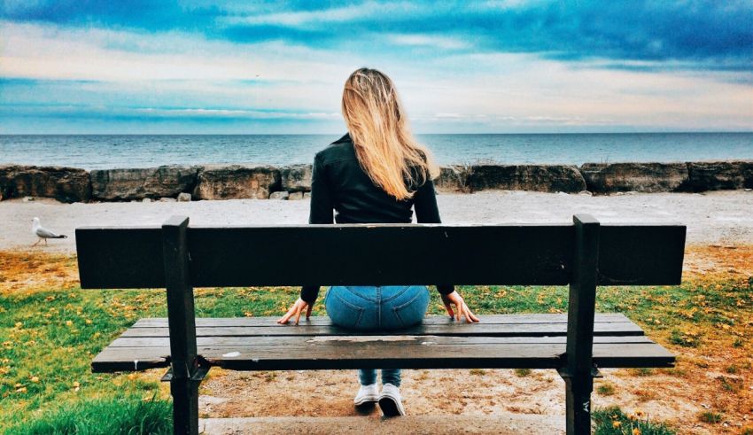 A woman sitting on a bench looking at the ocean.