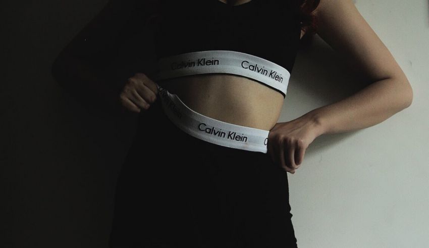 A woman in a black bra and shorts posing in front of a wall.