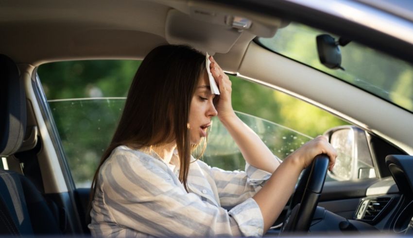 A woman is driving a car with her hands on her head.
