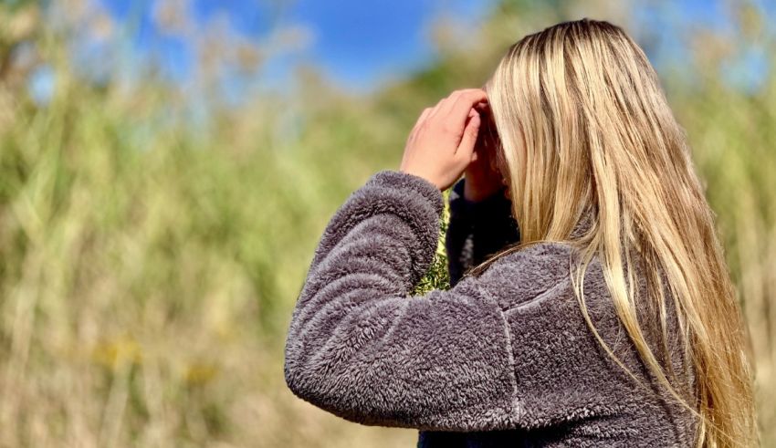 A woman with long blonde hair standing in tall grass.