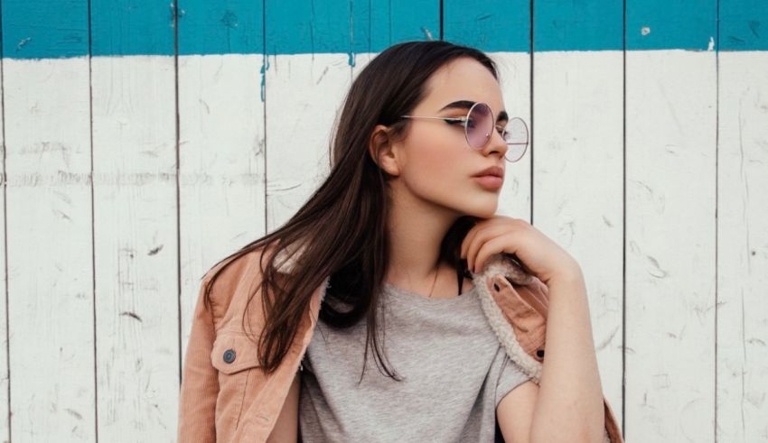A young woman in a pink jacket leaning against a wooden wall.