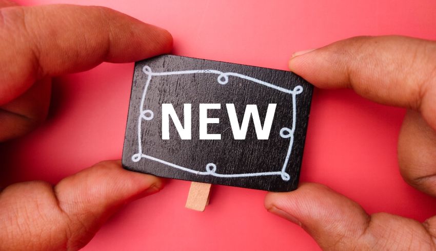 A hand holding a sign with the word new on it.