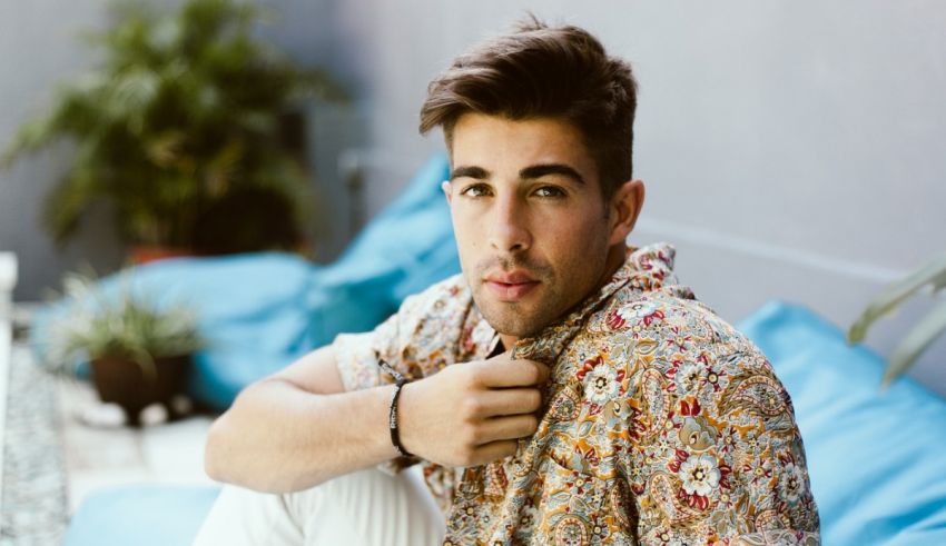 A man in a floral shirt sitting on a blue couch.
