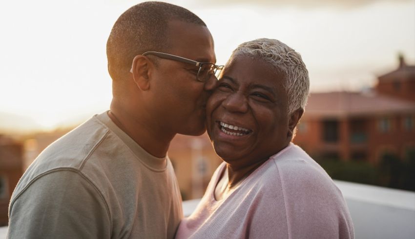 A black man and woman kissing in front of a building at sunset.