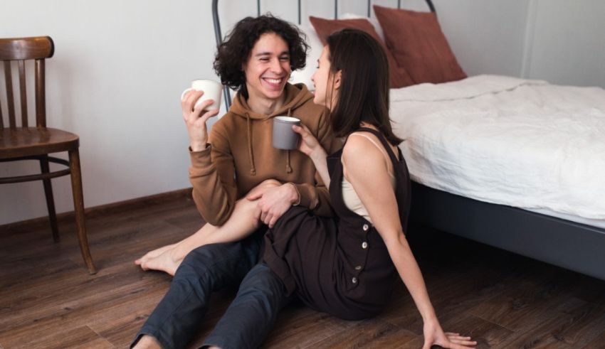 A man and woman are sitting on the floor in their bedroom.