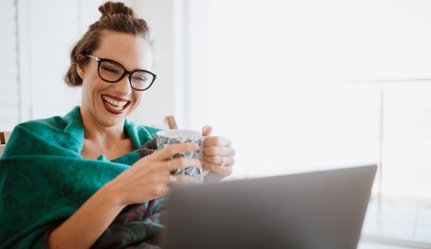 A woman is holding a cup of coffee while working on her laptop.