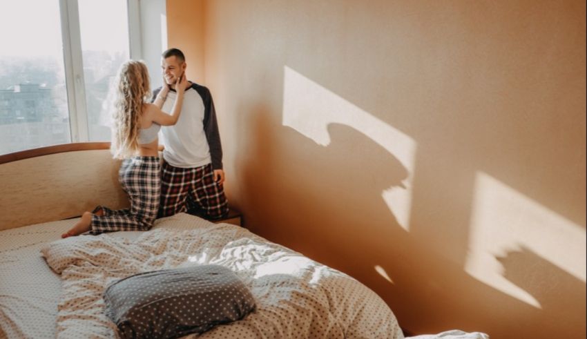 A couple in pajamas standing on a bed in front of a window.