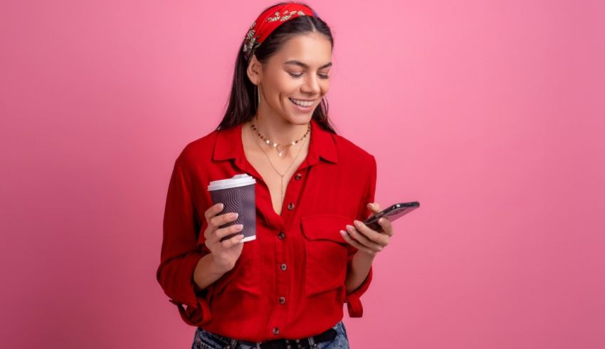 A young woman is holding a cup of coffee and looking at her phone.
