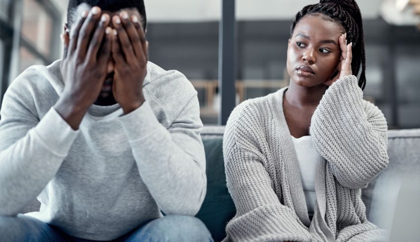 A man and woman sitting on a couch with their hands covering their faces.