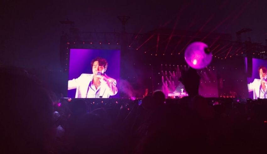 A group of people at a concert with a large screen.