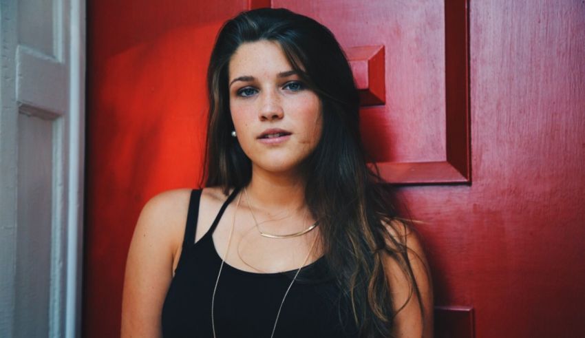 A young woman leaning against a red door.