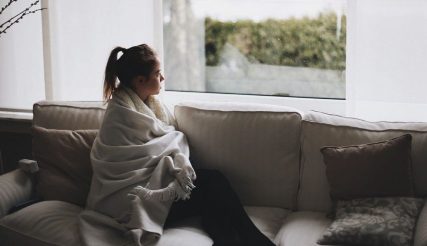 A woman sitting on a couch with a blanket wrapped around her.