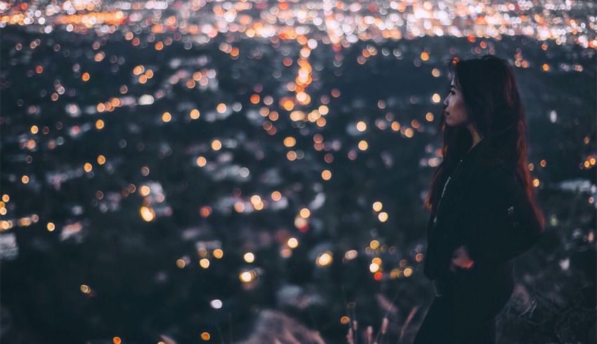 A woman standing on a hill overlooking a city at night.