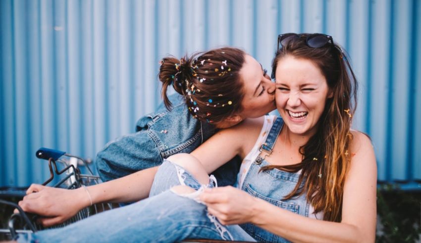 Two women sitting on a bicycle with confetti in their hair.