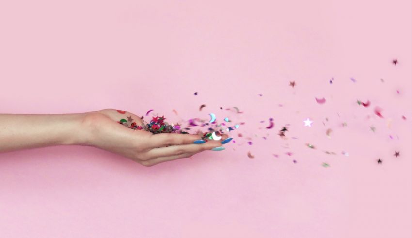 Confetti falling from a woman's hand on a pink background.