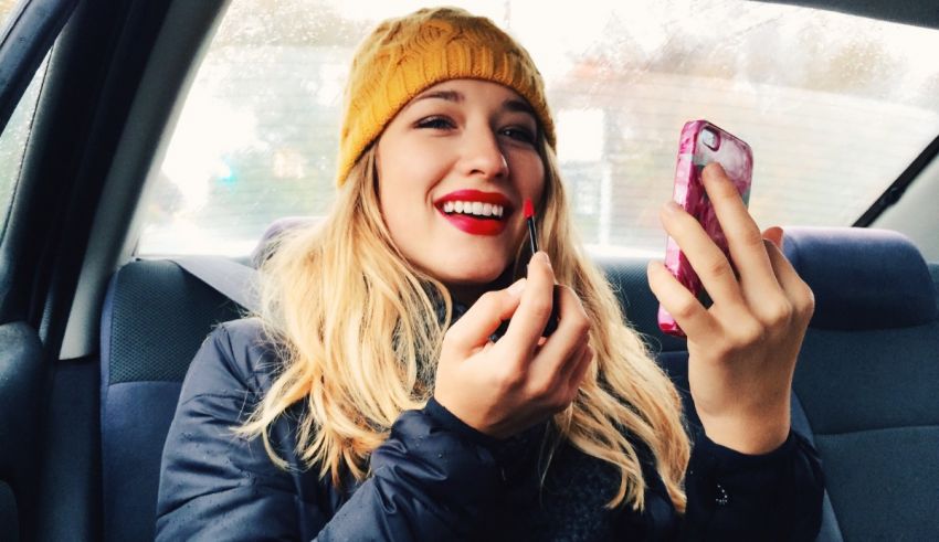 A woman in a yellow beanie is brushing her teeth in a car.