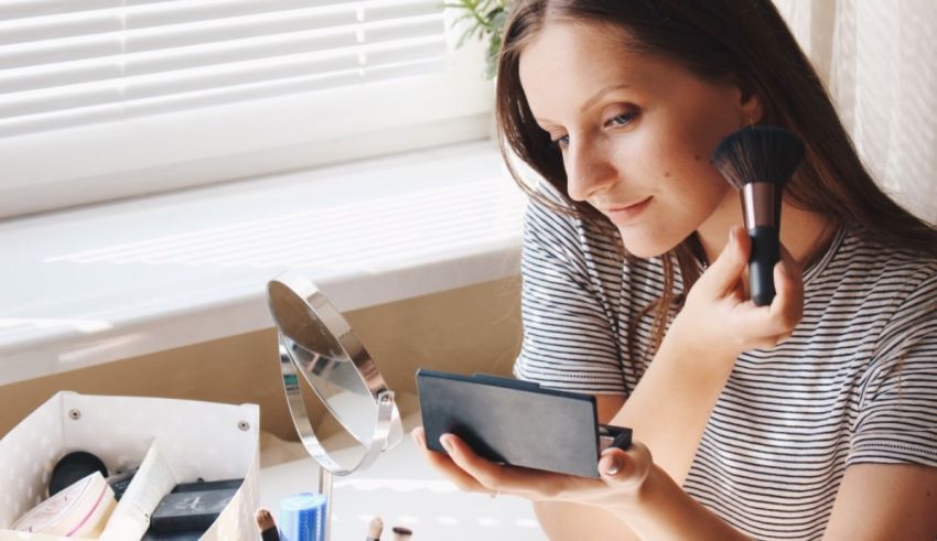 A woman is using a makeup brush in front of a mirror.