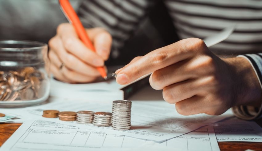 A person is holding a pen and a stack of coins on a table.