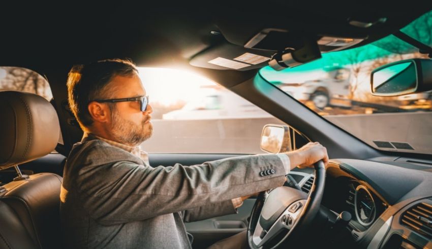 A man driving a car with sunglasses on.
