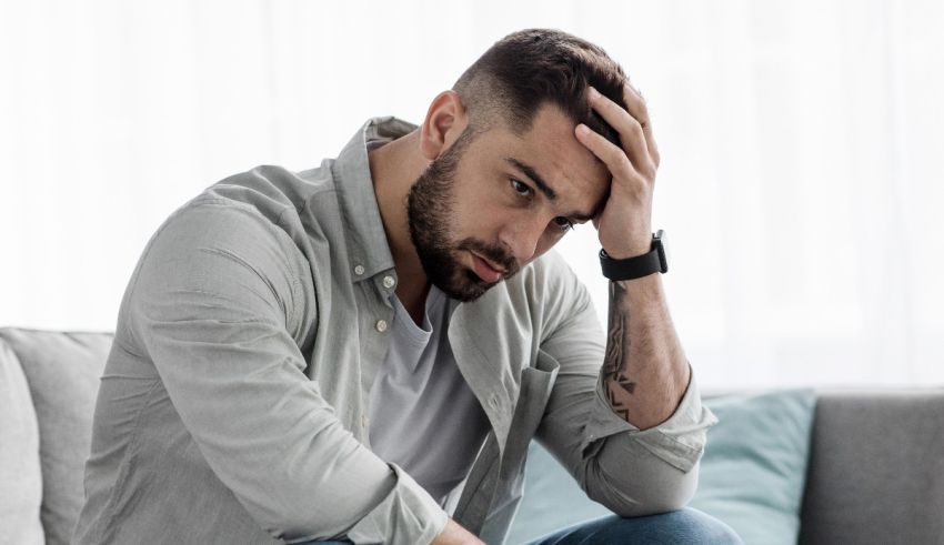 A man sitting on a couch with his hand on his head.