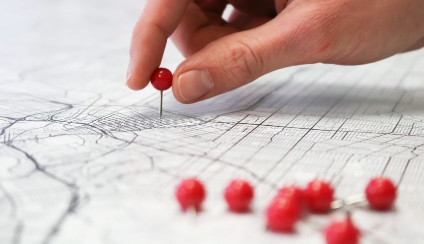 A hand pointing at a map with red pins.