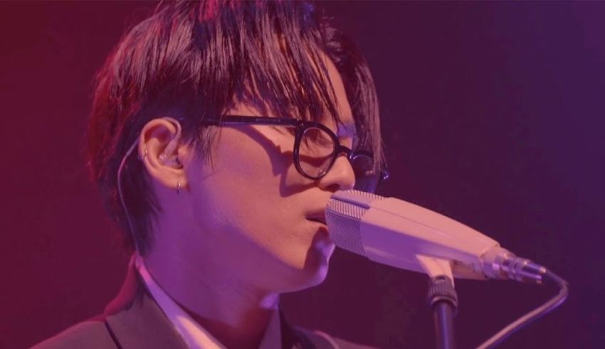 A man in glasses is singing into a microphone.