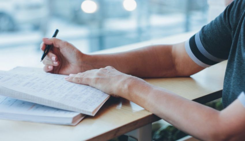 A man writing in a notebook with a pen.
