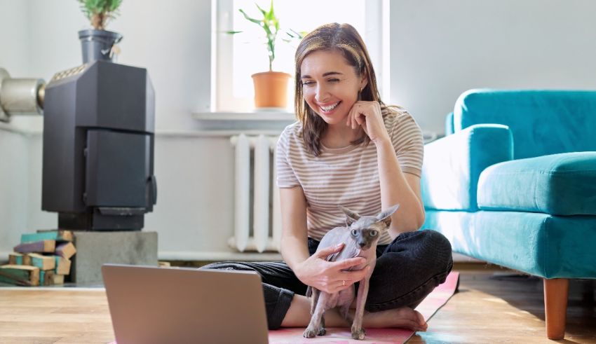 A woman sitting on the floor with a cat and a laptop.