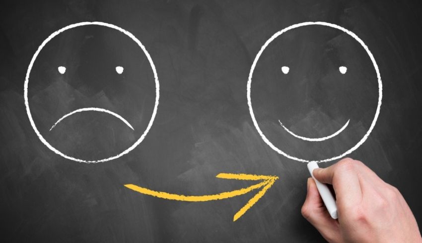 A hand drawing a happy and sad face on a blackboard.