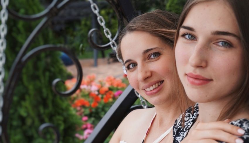 Two young women sitting on a swing in a garden.