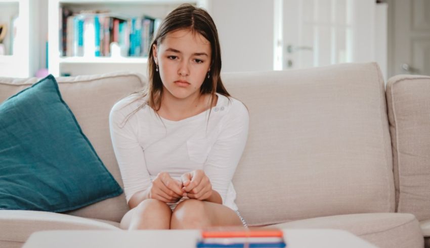 A young girl sitting on a couch with a book in front of her.