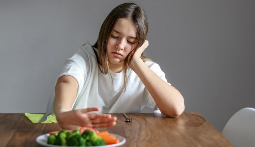 A woman sitting at a table with a plate of broccoli.