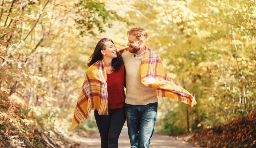 A couple walking in the woods with a blanket on their shoulders.