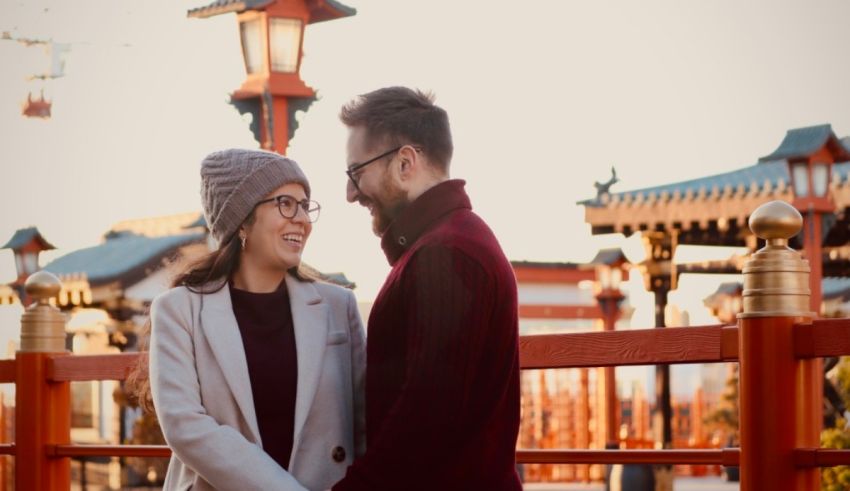 A couple is standing on a bridge in front of a japanese temple.