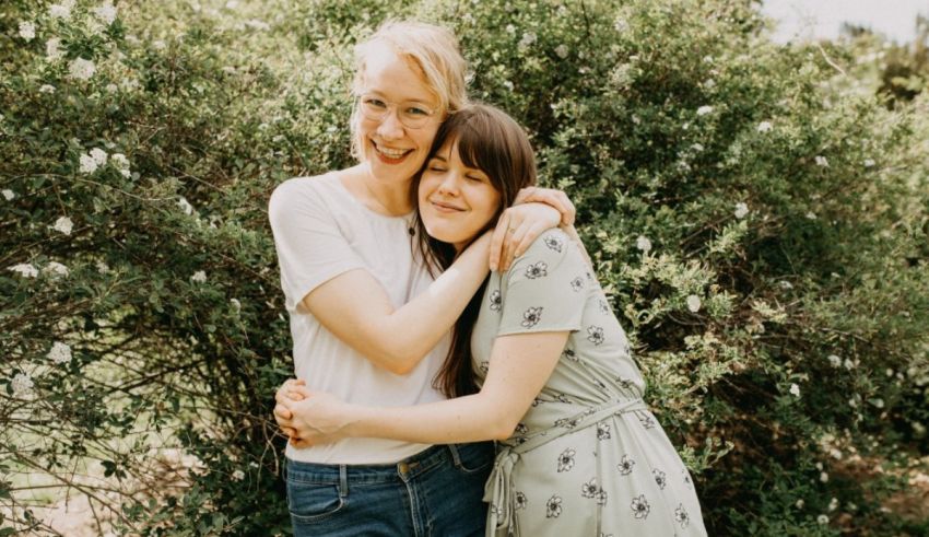 Two women hugging in front of bushes.