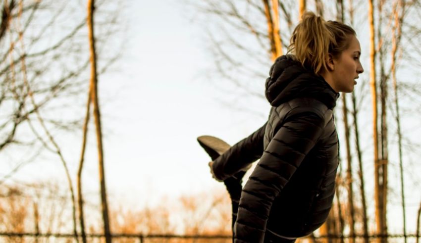 A woman in a black jacket is doing a handstand in a park.