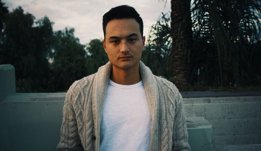 A young man wearing a white sweater and cardigan.