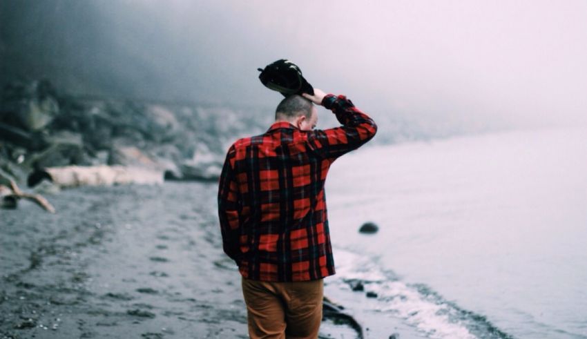 A man wearing a plaid shirt walking on the beach.