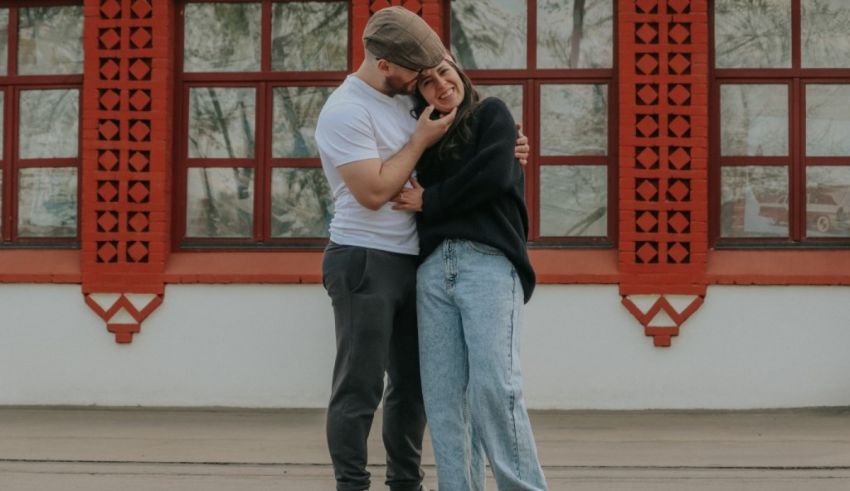 A man and woman hugging in front of a red building.