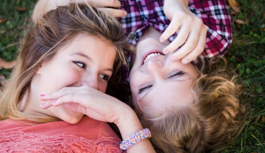 Two girls laying on the grass and smiling at each other.
