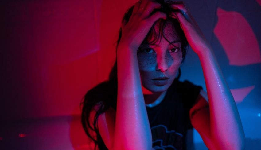 A woman with her hands on her head in front of a red and blue light.