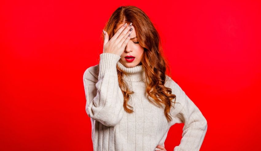 A young woman covering her eyes with her hands on a red background.