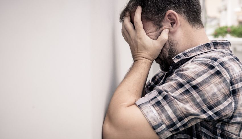 A man leaning against a wall with his hand on his face.
