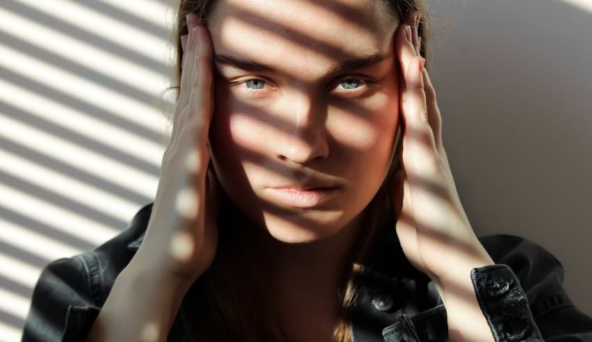 A woman with her hands on her head in front of a window.