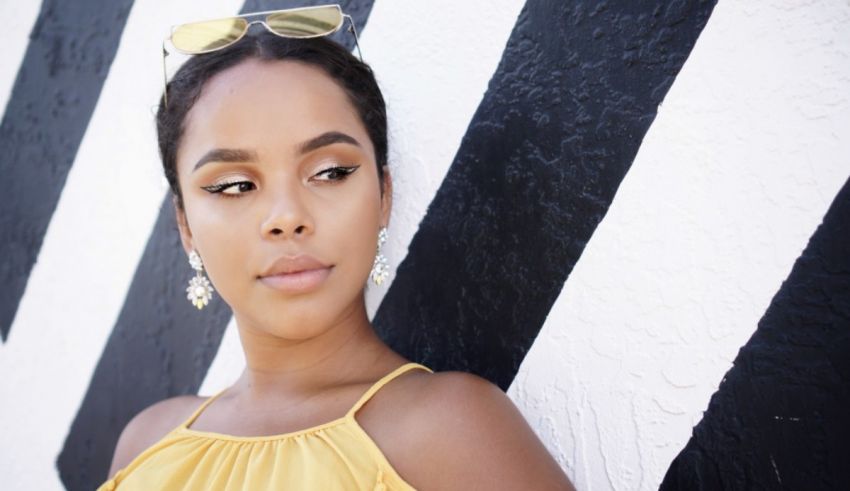 A black woman in a yellow dress leaning against a black and white wall.
