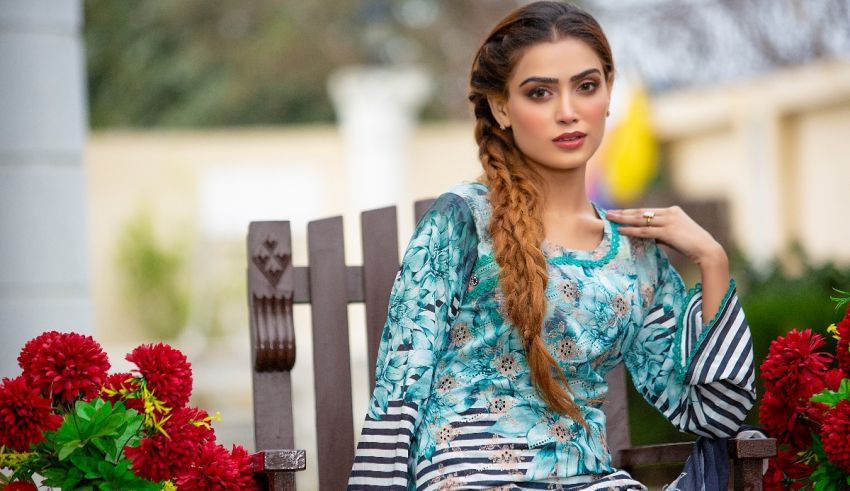A beautiful woman sitting on a bench in front of flowers.